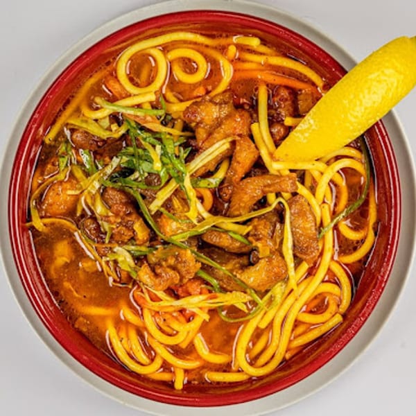 Togo India's chicken noodle soup with green onions and a lemon wedge in a red bowl.