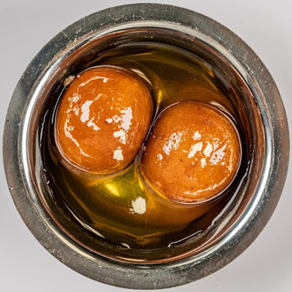 Two gulab jamun, Indian fried dough balls, soaking in syrup in a metal bowl.